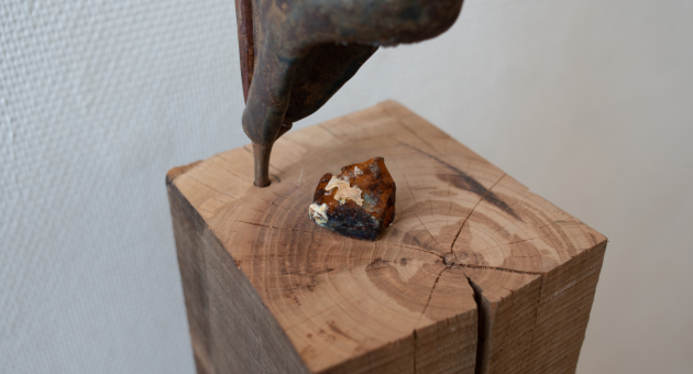 Een metalen beeldhouwwerk bovenop een houten blok met een mineraal