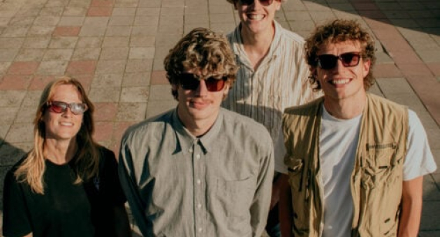 Vier bandleden van THE VELCRO poseren lachend in de zon, met zonnebrillen en een surfachtige uitstraling. De ontspannen sfeer en hun styling ademen de speelse energie van een surfcultuur.