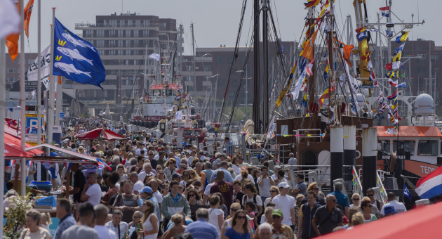 Vlaggetjesdag Scheveningen met een haven vol zomers geklede mensen en boten versierd met vlaggetjes. 