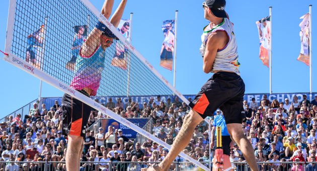 Twee spelers tijdens een beachvolleybalmatch, met publiek op de achtergrond.