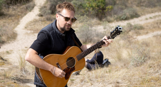 Een man met een gitaar speelt muziek in de duinen.