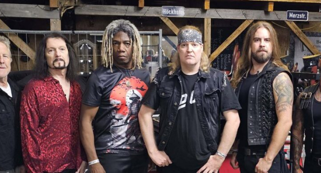 Zes muzikanten van Warlord in zwarte kleding, poseren samen.