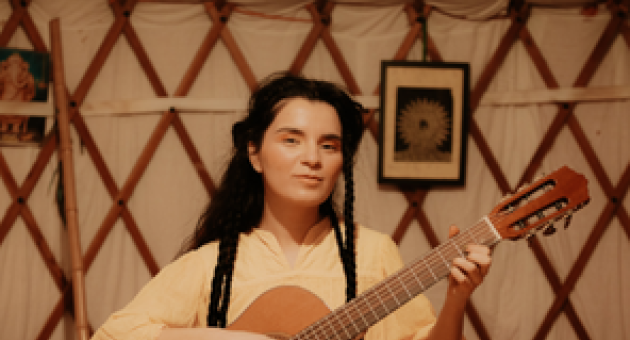 Meisje met lange vlechten in wit gewaad speelt op een akoestische gitaar