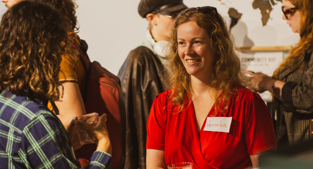 Een vrouw met krullend haar in een rode jurk glimlacht op een evenement.