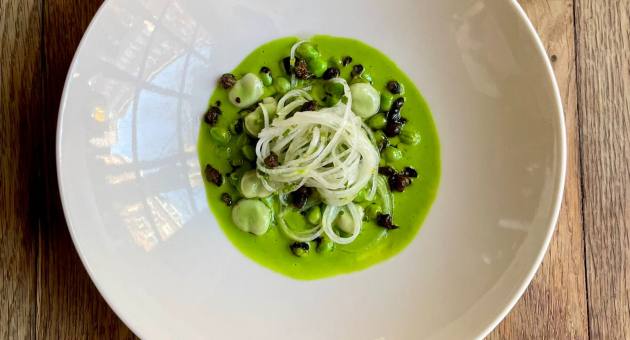 Een mooi gepresenteerd gerecht met groene puree, uien en bonen op een witte bord.