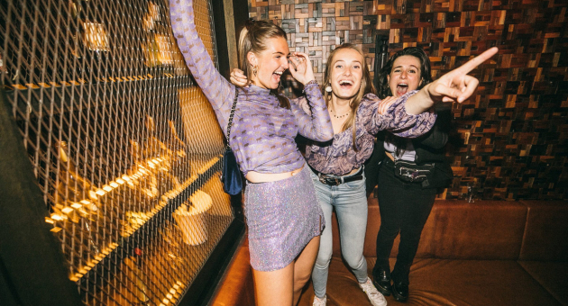 Drie lachende vrouwen staan in een club en vieren.