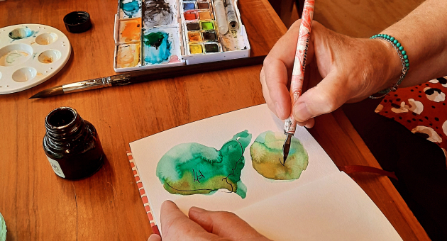 Een hand schildert groene aquarel vlekken in een notitieboek.