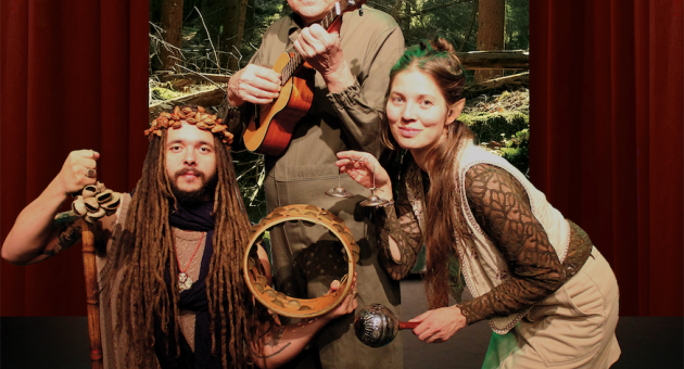 Drie mensen poseren in een bosomgeving, met muziekinstrumenten.