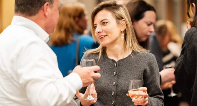 Een vrouw met blonde haren praat met een man op een evenement.