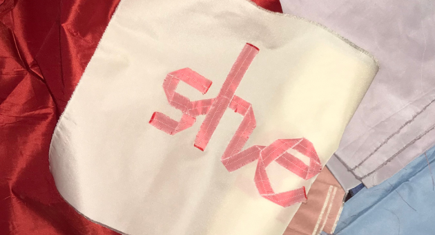 Een vlag met de woorden 'she' in roze op een witte achtergrond.