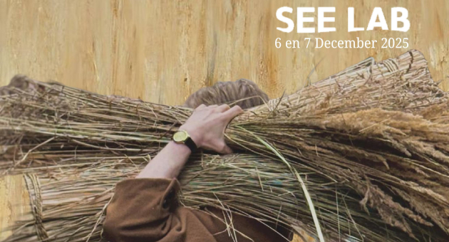 Foto van een man in een bruine pij in een korenveld met een bos graan op zijn schouder