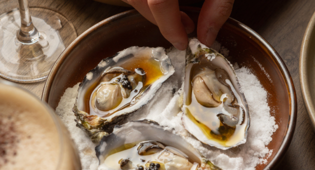 Hand van iemand die een oester uit een schaal pakt.