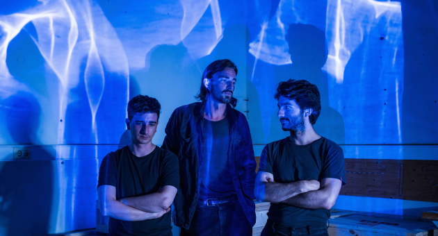 Drie mannen staan naast elkaar met blauwe lichtprojecties.