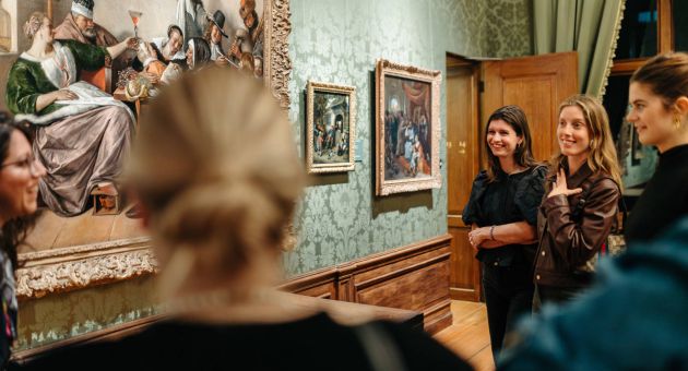 Een groep mensen bekijkt een schilderij in een museum.