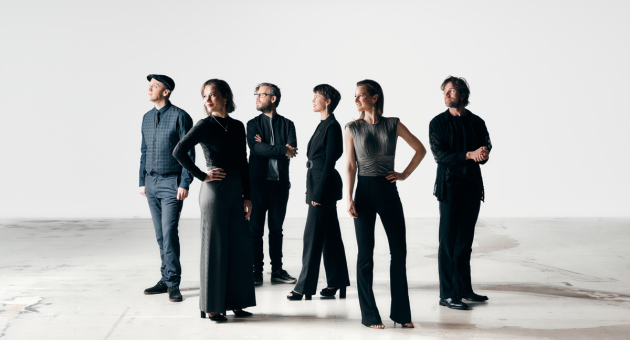 Zes mensen in zwart gekleed staan in een lege ruimte.