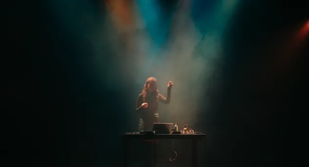 Een vrouw met lange haren staat achter een tafel met DJ-apparatuur.