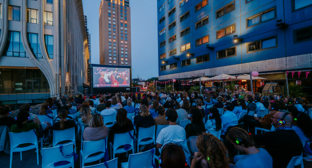 A crowd watching a film on a large screen outdoors.