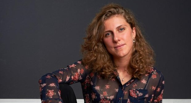 Een vrouw in een bloemenoverhemd zit met een gitaar.