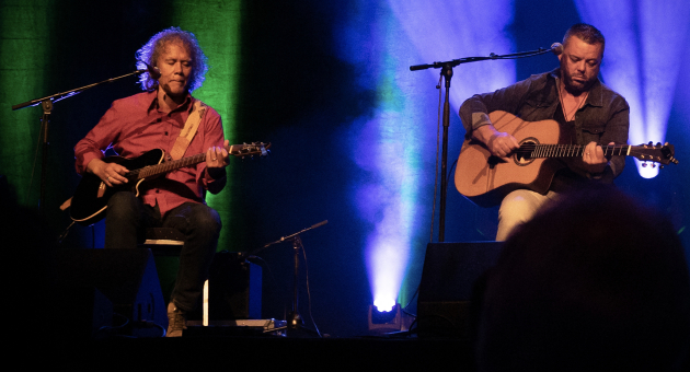 Twee gitaristen op een sfeervol verlicht podium