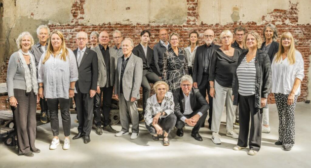 Een groep van twintig mensen posed voor een muur.