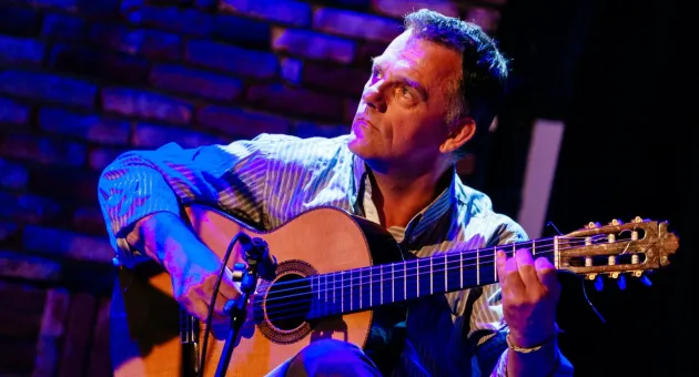 Componist en gitarist Kees Gelderblom met akoestische gitaar voor een microfoon