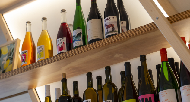 Een assortiment wijnflessen in diverse kleuren op een houten plank.