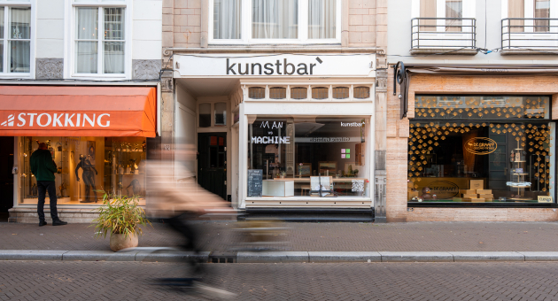 Een drukke straat met winkels en een fietser die passeert.