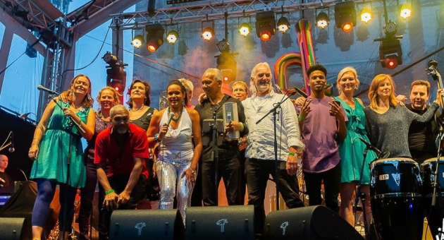 Groep muzikanten op het podium tijdens een optreden, met microfoons en instrumenten.