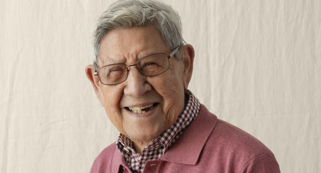 Een oudere man met grijs haar en een bril glimlacht naar de camera.