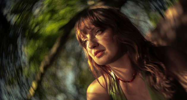 Portret van singer songwriter Madison Cunningham. Ze staat bij een boom en het zonlicht valt op haar gezicht