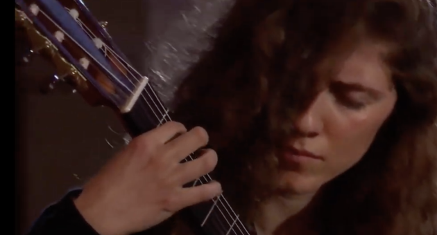 Een vrouw met krullend haar die geconcentreerd gitaar speelt.