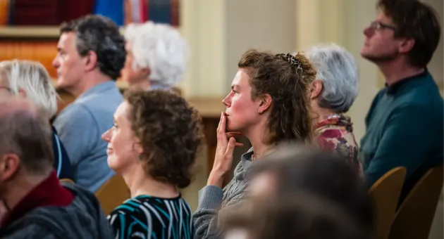 Mensen zittend in een zaal die aandachtig naar iets of iemand luistern. 