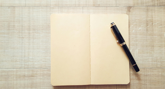 Een leeg notitieboek ligt open naast een zwarte pen.