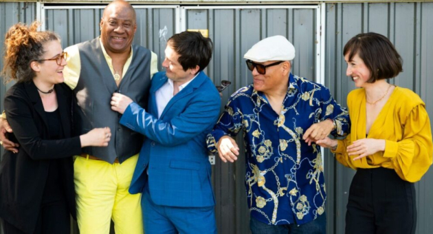 Vijf mensen lachen en poseren samen in een casual setting.