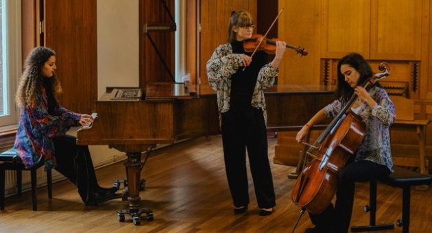 De drie muzikanten van Piano Trio Lyria met een vrouw zittend achter piano, met een cello en een vrouw staand met een viool