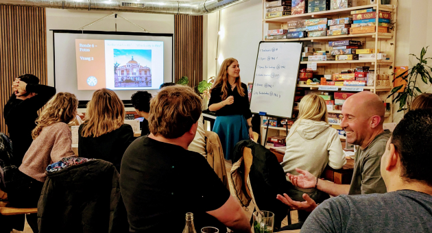 Een groep mensen kijkt naar een presentator tijdens een quizavond.