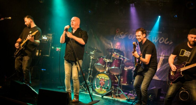 Bandoptreden op het podium. Vijf bandleden spelen live op een donker podium met kleurrijke lichten.