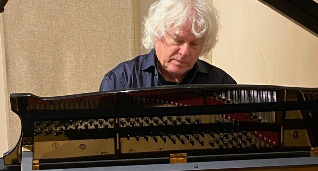 Een man met wit krullend haar speelt op een piano.