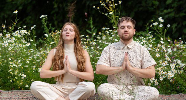 Twee mensen mediteren met samengevoegde handen in een bloemenveld.