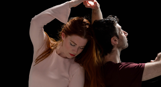 Een vrouw met lang, rood haar en een man met kort, donker haar dansen samen.