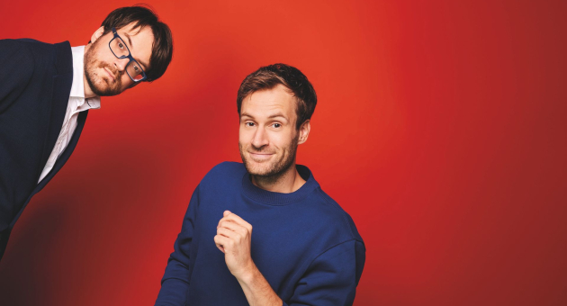Twee mannen poseren voor een rode achtergrond.