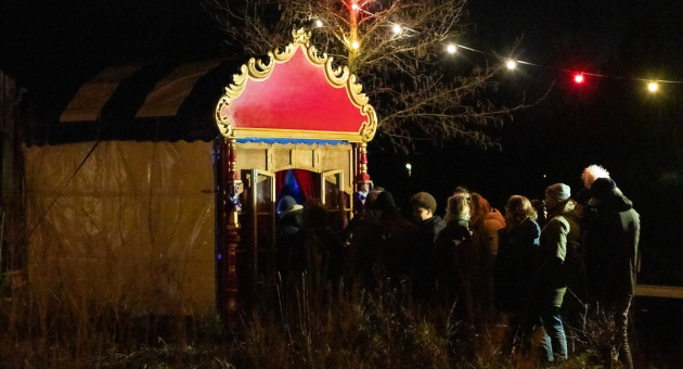 Mensen wachten in de nacht bij een kleurrijk poppentheater.