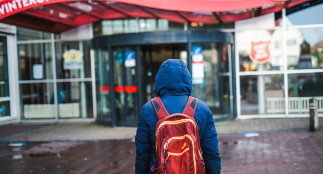 Persoon met blauwe jas en rode rugzak loopt richting ingang van winteropvang