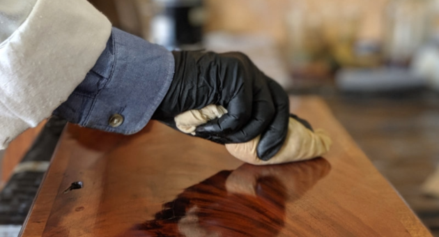 Hand in zwarte handschoen brengt olie of lak aan op glanzend houten oppervlak