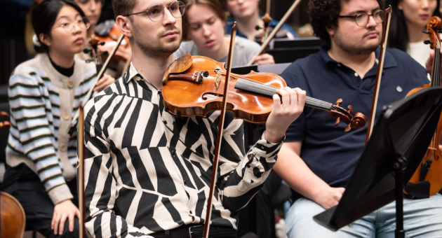 Jongeman met een viool zit in een orkestrepetitie.