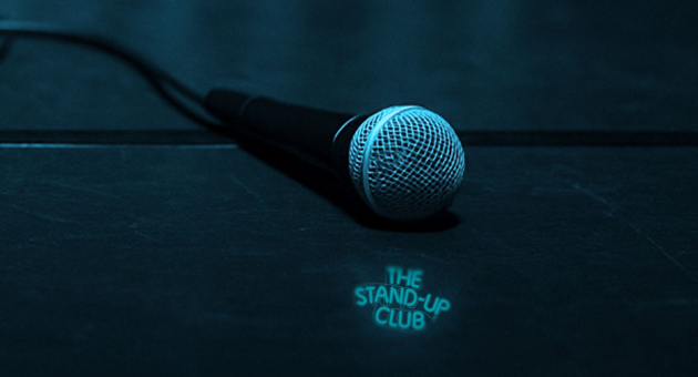 Microfoon liggend op een podium met de tekst: the stand-up club