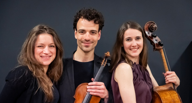 Drie musici poseren met viool en cello tegen een donkere achtergrond