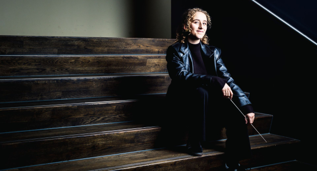 Dirigent Chloe Rooke met baton zittend op een trap.