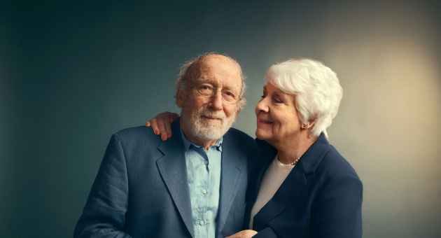 Oud stel in nette kleding met armen om elkaar tegen een donkere achtergrond