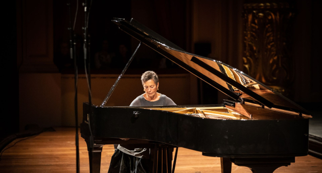 Pianist speelt op een vleugel op een sfeervol verlicht podium in een concertzaal.